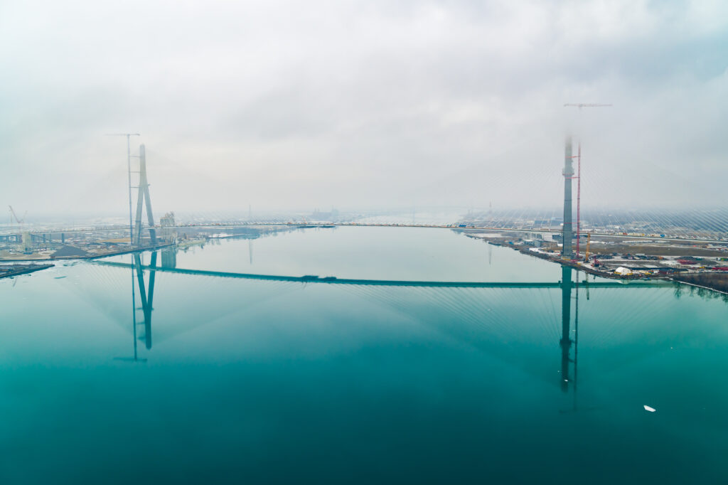 Horizontal view of full bridge with clouds around mast and mirror image in the river